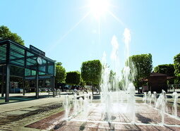 Ein beeindruckender Springbrunnen in der Mitte des Kurplatzes Bad Füssing bei strahlendem Sonnenschein.