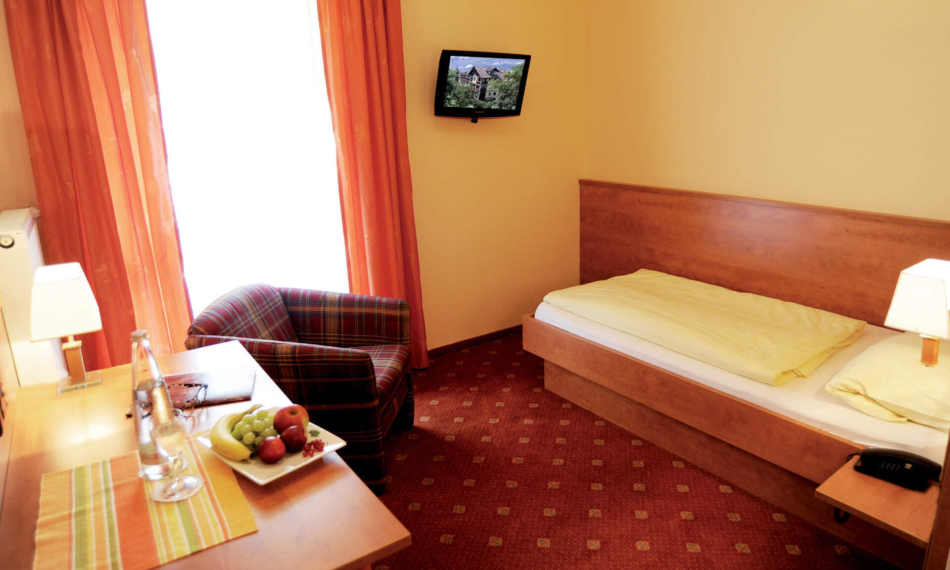 schlichtes Einzelzimmer mit Sessel neben dem Bett und Fernseher für entspannte Abende im Wellneshotel Richstein's Posthotel.