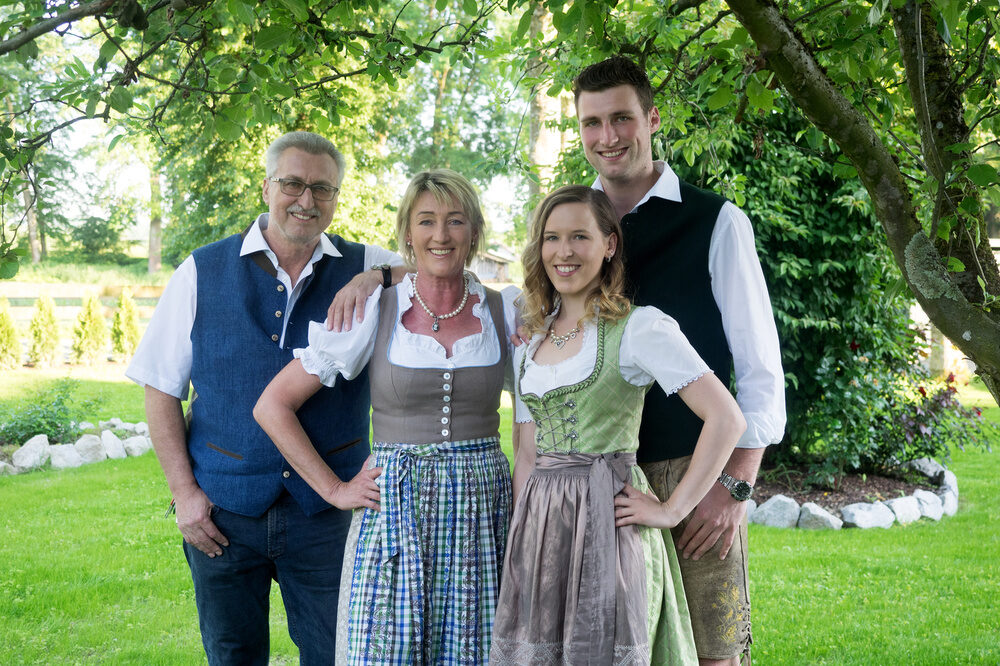Die Gastgeberfamilie steht lächelnd mit Trachten in dem grünen Garten im Richstein's Posthotel, Bad Füssing.