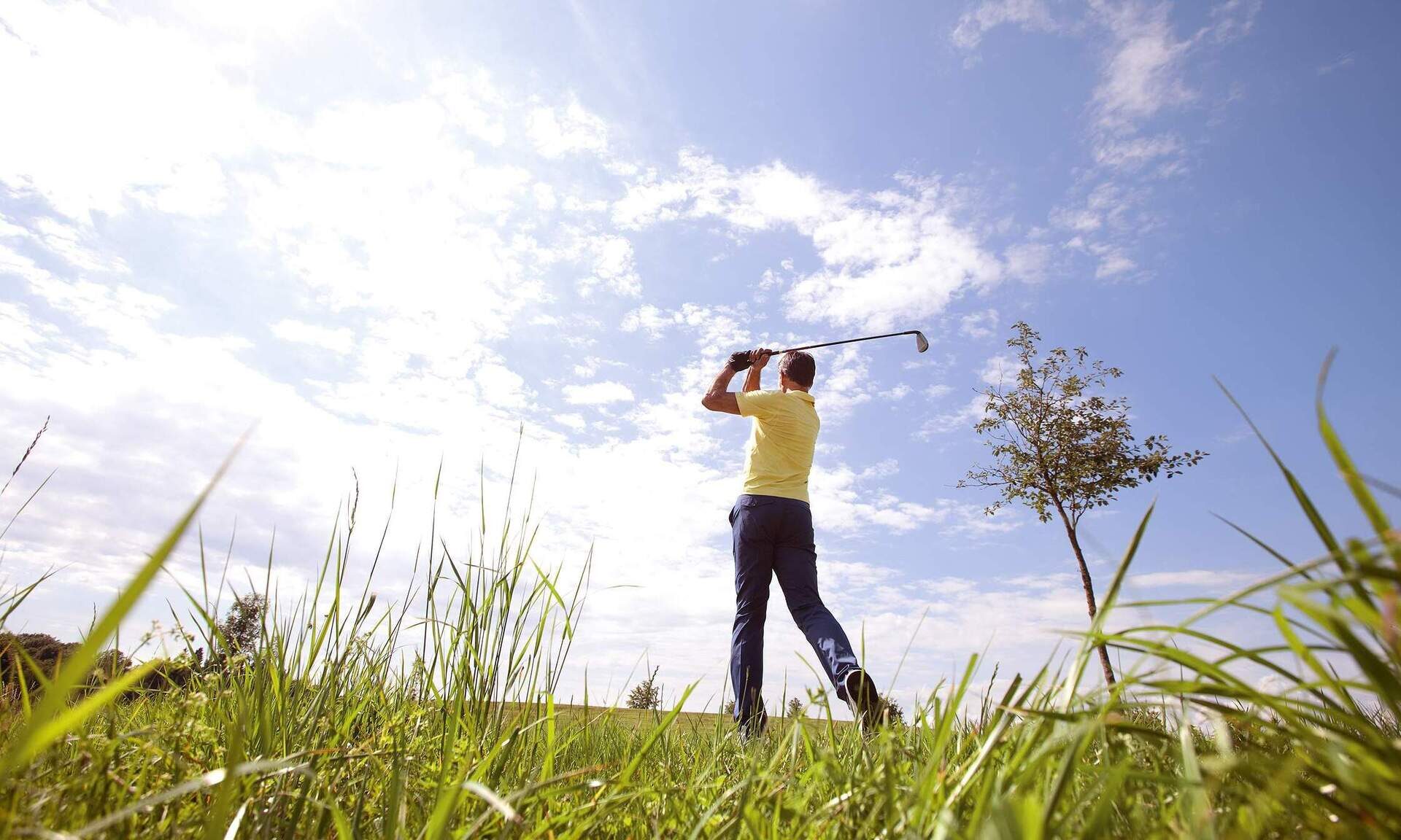 Ein männlicher Golfer, gekleidet in passender Kleidung, schwingt seinen Golfschläger auf einem sonnigen Golfplatz in Bad Füssing.