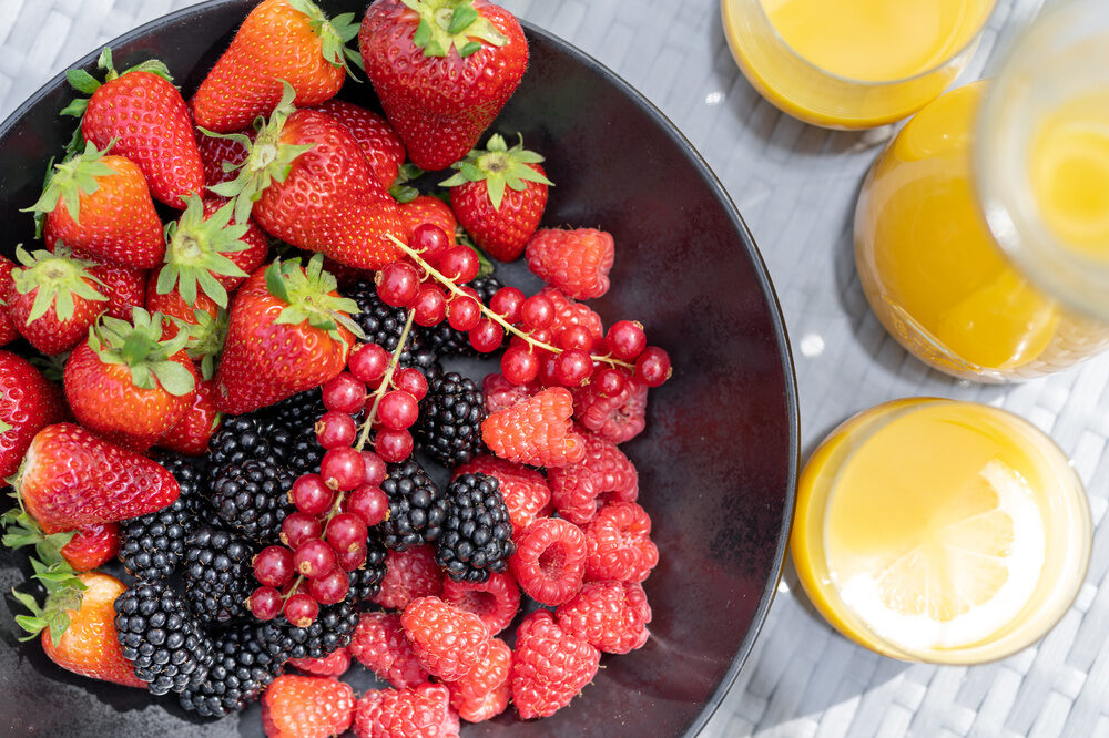 Ein Frühstückstisch auf der Terrasse im Wellnesshotel Richstein's Posthotel Bad Füssing mit einer Auswahl an Beeren und Saft.