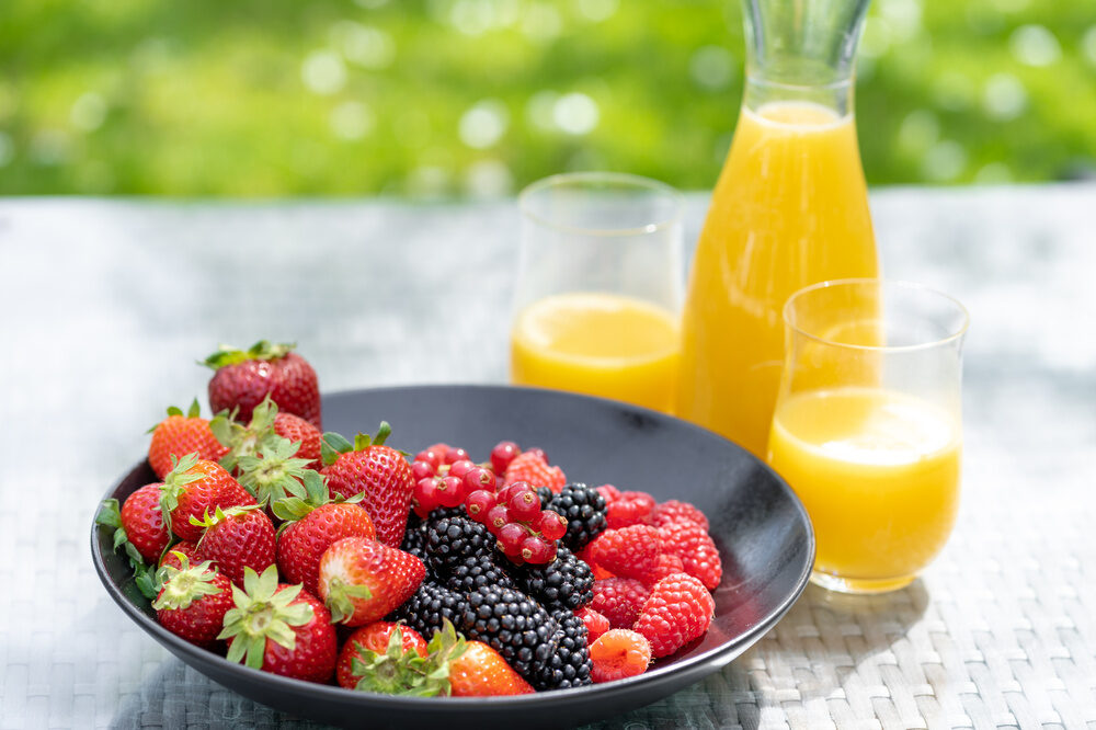 Ein Teller mit frischen Früchten und Orangensaft auf dem Tisch im Terrassen- und Gartenbereich des Richstein Postkurhotels.