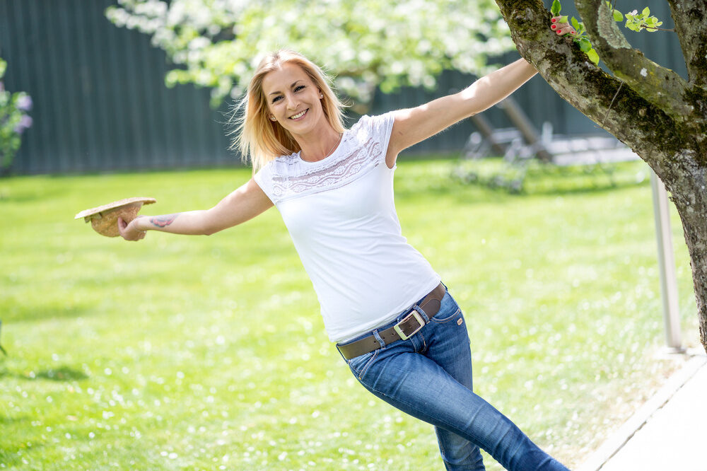 Die Frau hebt fröhlich eine Hand, die Leichtigkeit des Moments im Garten des Wellneshotels Bad Füssings einfangend.