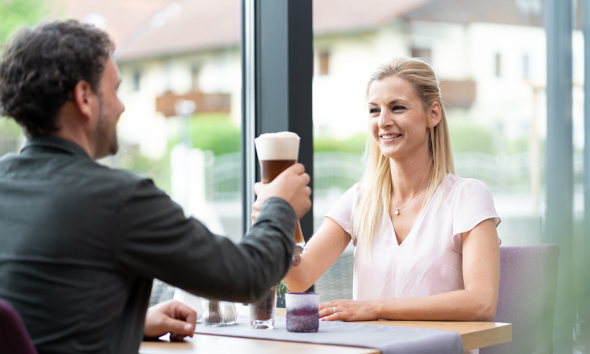 Ein Mann und eine Frau genießen ein Weizenbier an einem Fensterplatz der Terrasse des Restaurants Richstein's Posthotels.