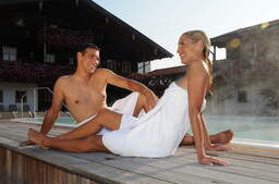 Zwei Menschen im Wellnessurlaub in Bad Füssing entspannen am Beckenrand eines Pooles einer Therme.