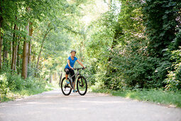 Ein Radfahrer in sportlicher Kleidung auf einem Fahrradweg durch den begrünten Wald in Bad Füssing.